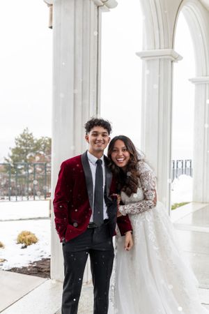 Cora Emilie Media -Winter wedding portrait with couple under white arched columns during snowfall.