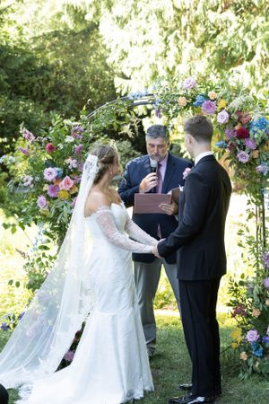 Cora Emilie Media An outdoor wedding ceremony under a floral arch with colorful summer blooms.