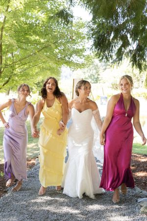 Cora Emilie Media Four women in colorful formal dresses walk together laughing on a garden path.