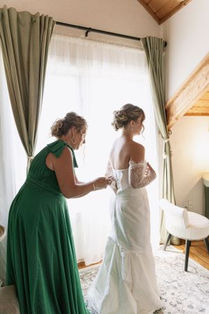 Cora Emilie Media Getting ready scene with emerald green and white dresses in a sunlit room.