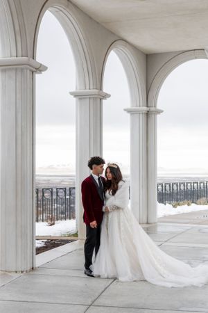 Cora Emilie Media -Elegant wedding couple posing under classical white archways in winter setting.