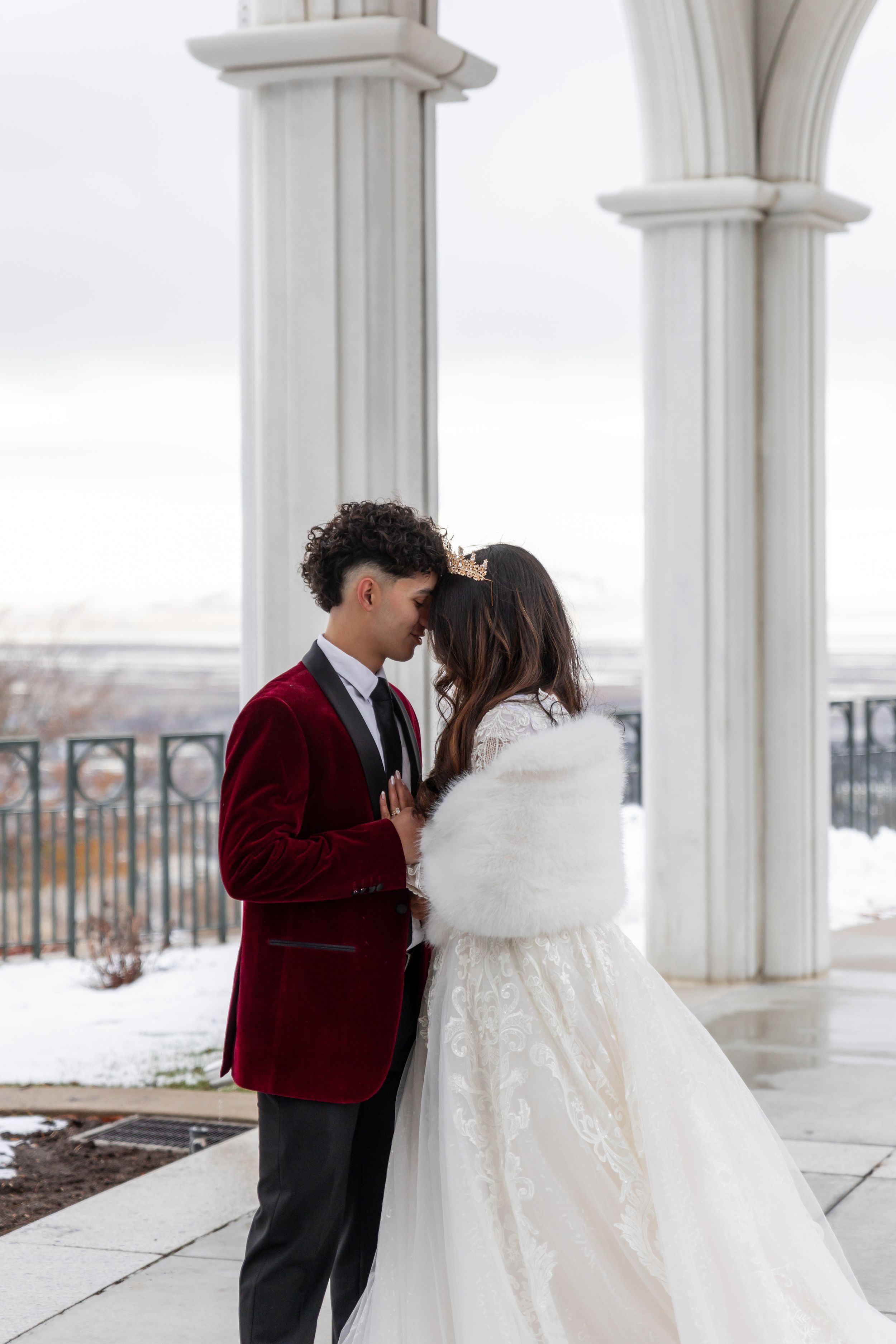Cora Emilie Media -A romantic winter wedding shoot featuring an elegant couple in burgundy velvet and white lace against white columns.
