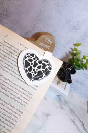 Book pages with cow print heart sticker against marble background with greenery.