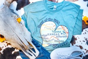 Light blue t-shirts with Kansas-themed graphic designs laid flat.