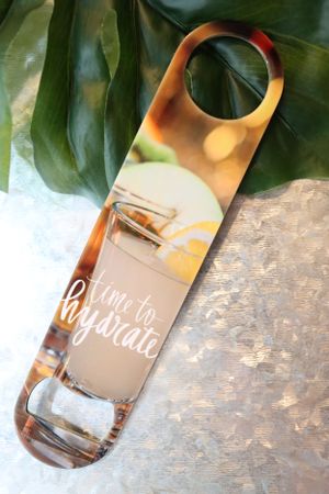 Glass wine bottles with elegant calligraphy text displayed under tropical leaves.