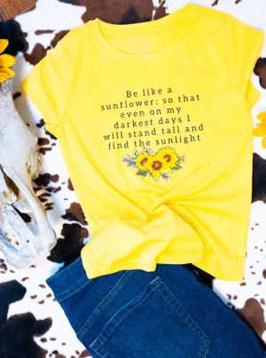 Yellow t-shirts with sunflower designs and inspirational quotes laid flat against dark background.