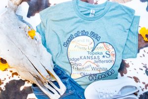 Light blue t-shirts with Kansas-themed designs and text laid out on display.