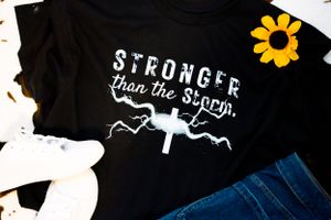 Black t-shirts with motivational text and storm cloud designs displayed on dark surface.