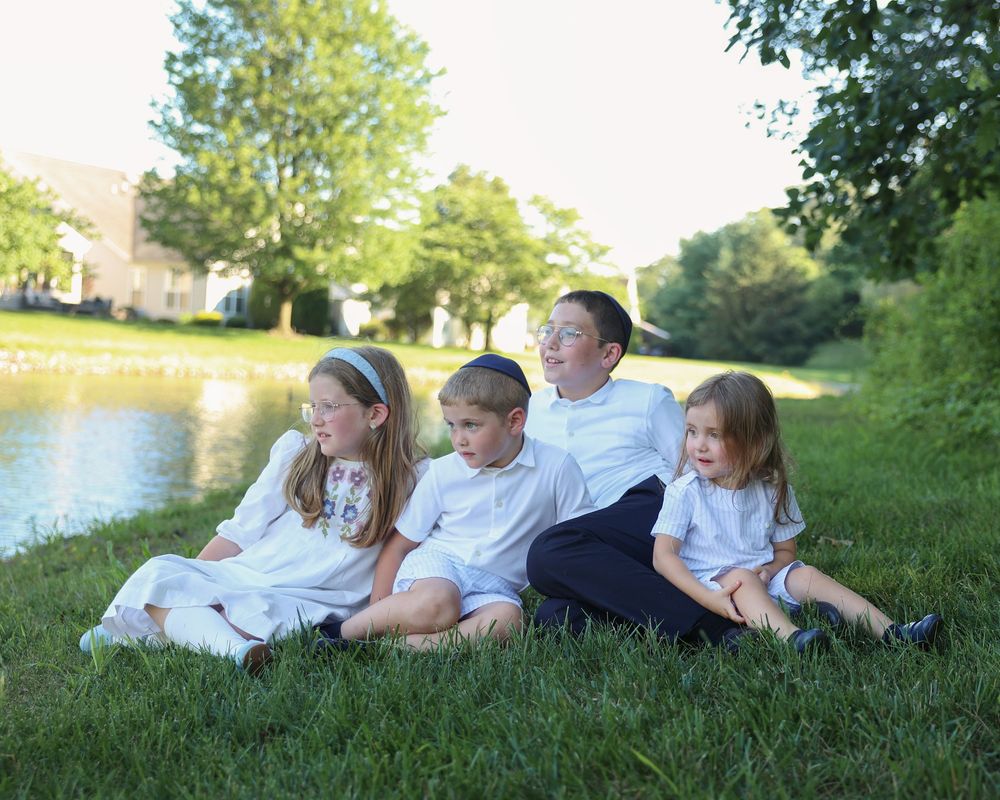 siblings sitting on the grass by a pond during a professional outdoor children's photography session in Lakewood