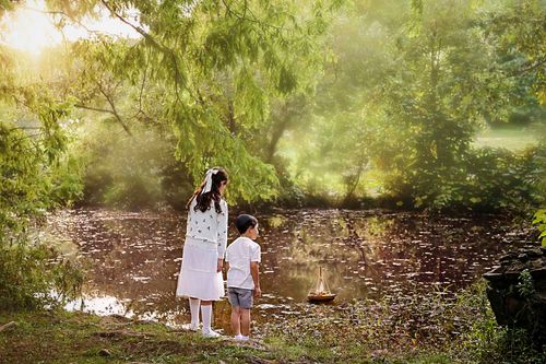 fine art portrait of siblings standing near a pond looking on at their toy boat floating in Deep Cut Gardens, Monmouth county NJ