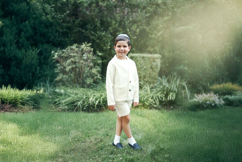 fin art natural light portrait of a young boy wearing a white suit posing in a garden