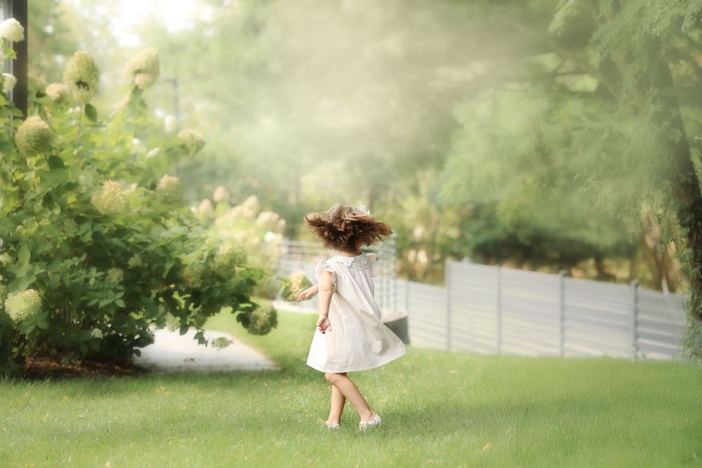 candid fine art photo of a young girl spinning in the grass with her hair flying in the wind