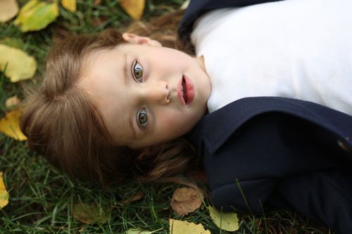 Detailed headshot of a child with hazel eyes looking directly up at the camera while lying outdoors