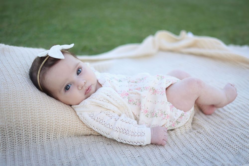 adorable infant girl wearing a big bow in her hair, lying on a knot blanket