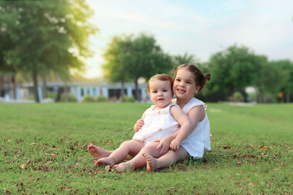 toddler sisters sitting in the grass with sun glow in the background