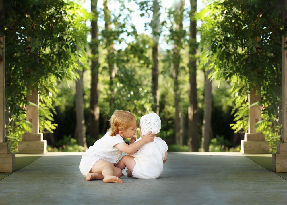 toddler siblings share a sweet moment in the scenic, summer greenery