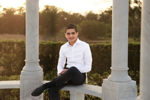 A professional outdoor portrait of a teenage boy sitting in a stone gazebo during golden hour