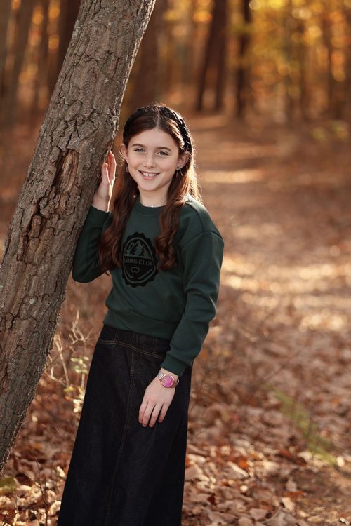 Portrait of a bas mitzva girl leaning on a tree with a blurred background of golden autumn trees and foliage
