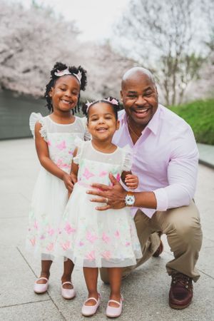 Smiling family in matching white dresses under spring cherry blossom trees at an outdoor park.