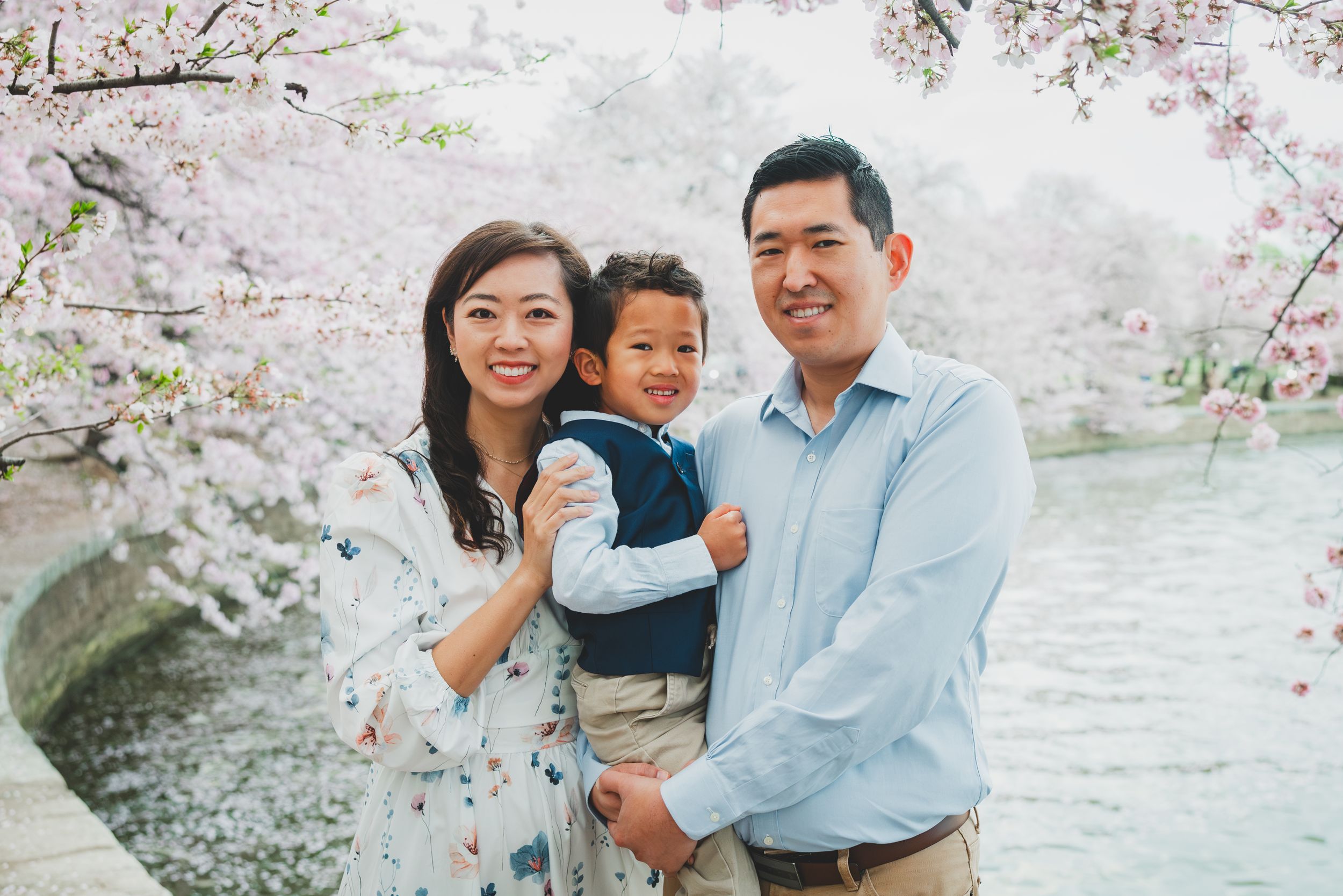 A family enjoying spring cherry blossoms together near a lake on a beautiful sunny day.