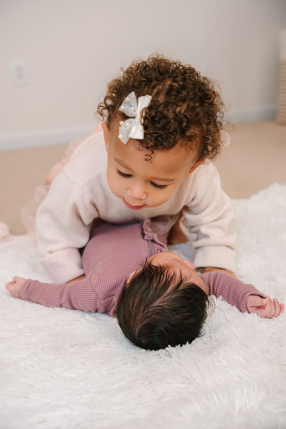 Two siblings share a tender moment together on a white fluffy blanket in a warm, natural light setting.