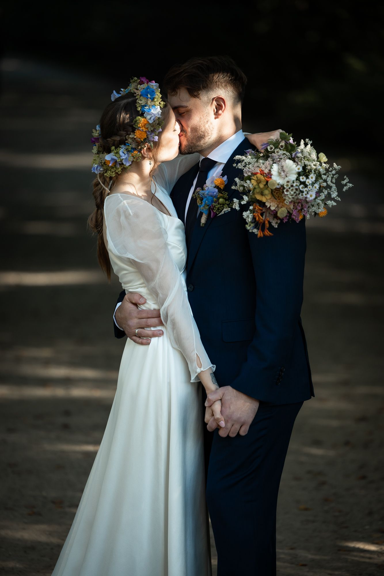 A romantic wedding couple share a kiss in a forest setting with the bride wearing a floral crown and holding a bouquet.