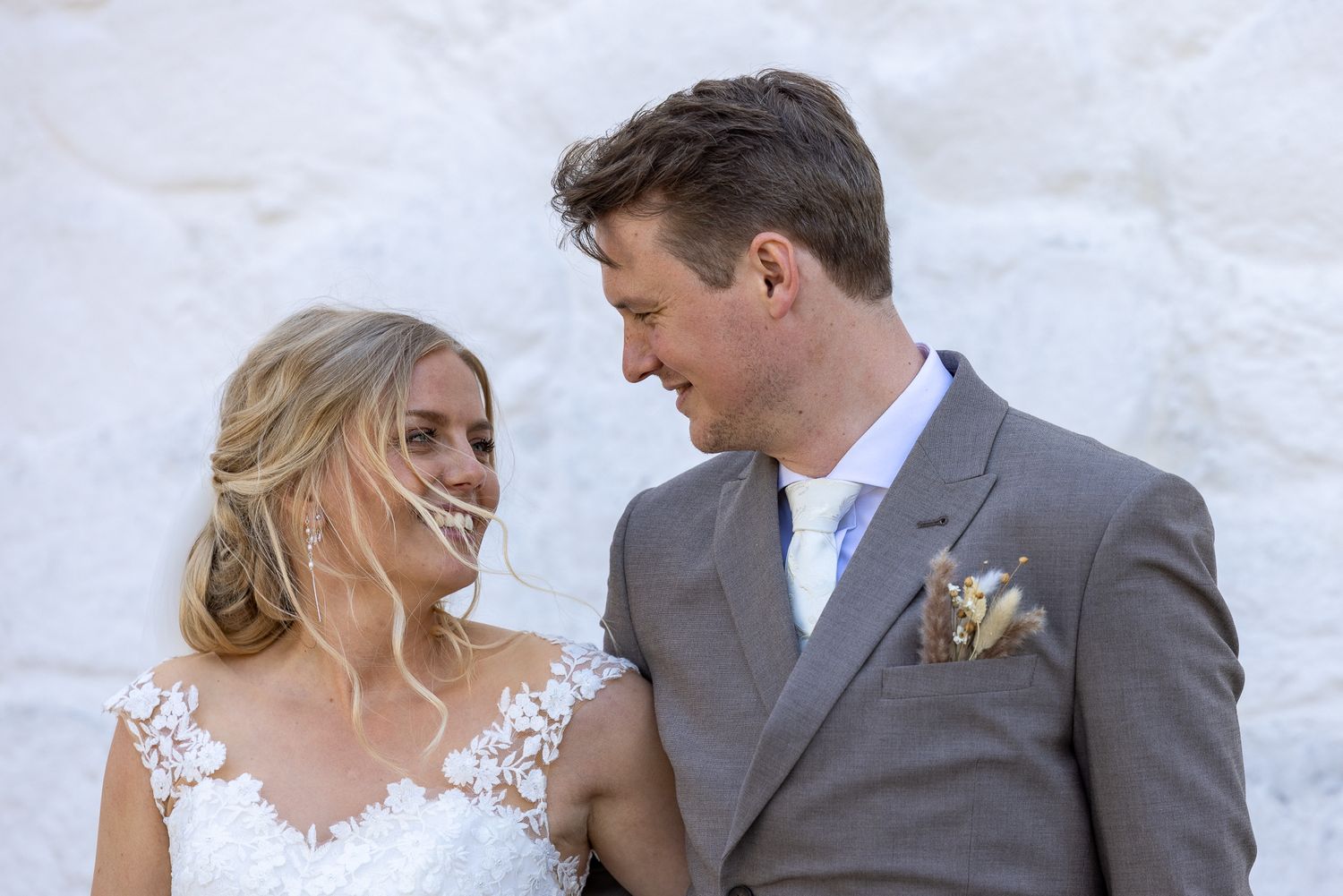 Wedding couple sharing a joyful moment against white wall backdrop.