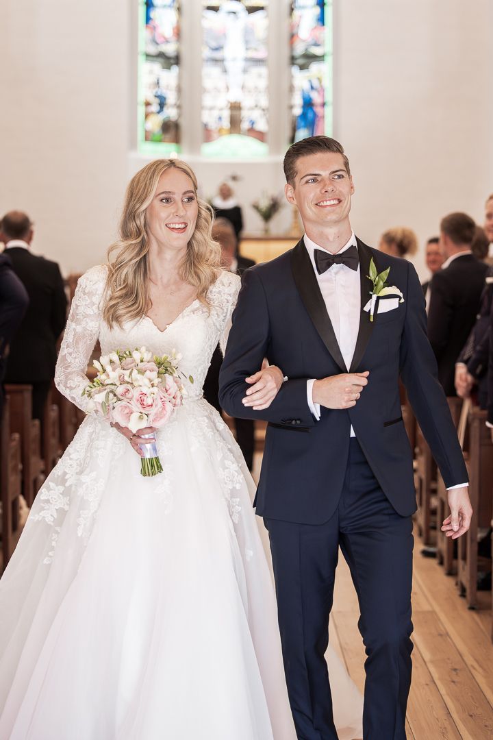 Couple walking down church aisle after ceremony with beautiful stained glass windows in background.