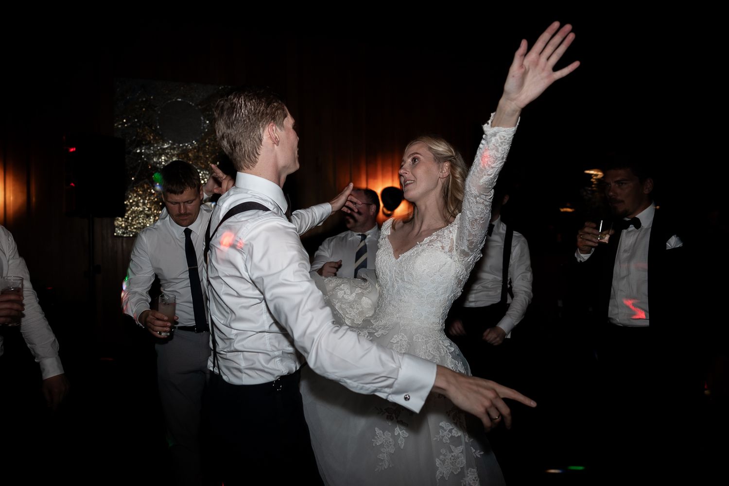 Couple dancing energetically at wedding reception party in dimly lit venue.