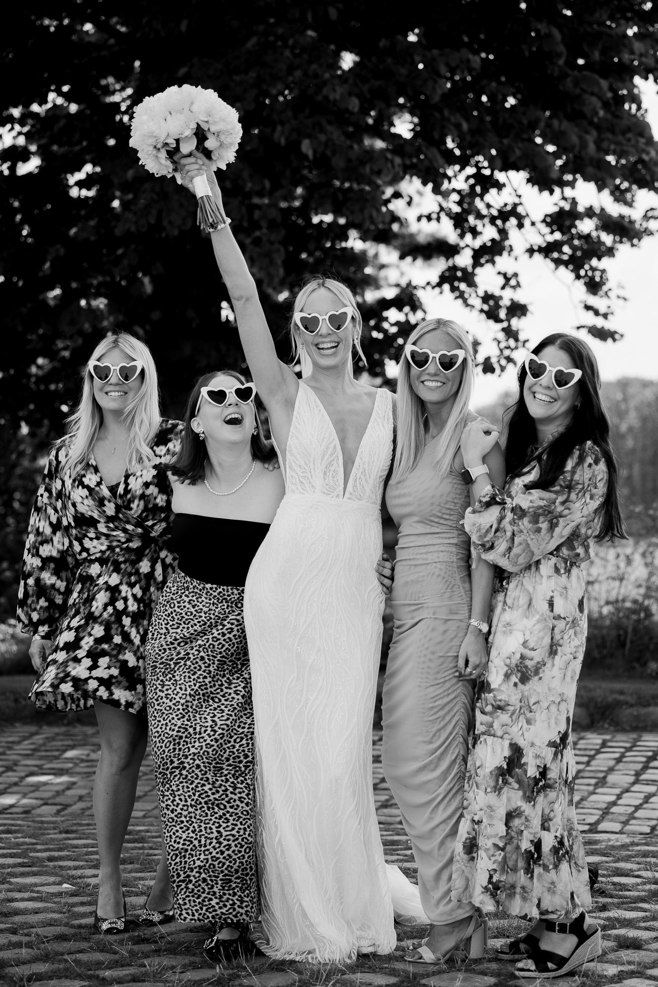 Wedding party in sunglasses posing together with bouquet raised in celebration.