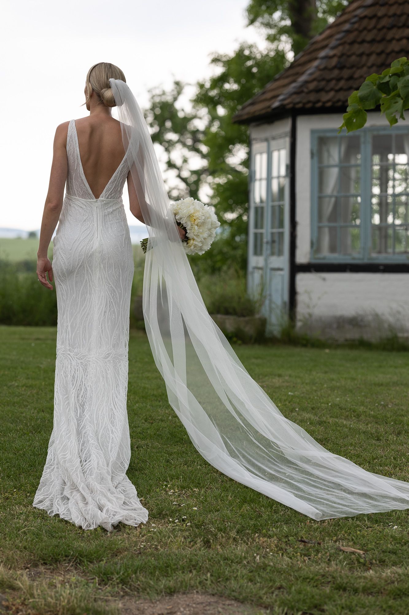 A wedding dress with plunging back and flowing train photographed against rustic garden scenery.