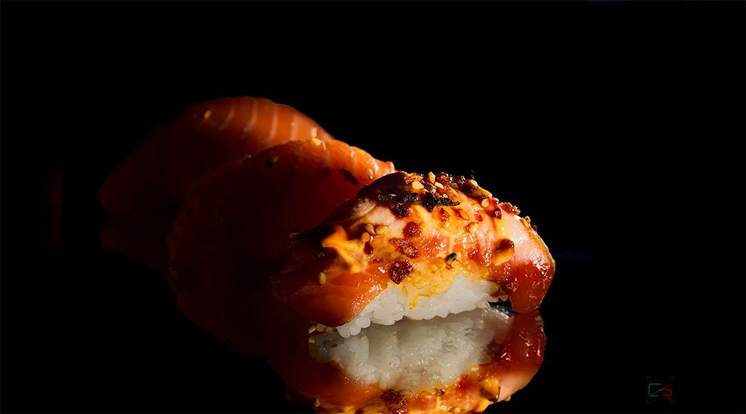 Three pieces of nigiri sushi with salmon and spicy toppings on a dark reflective surface.