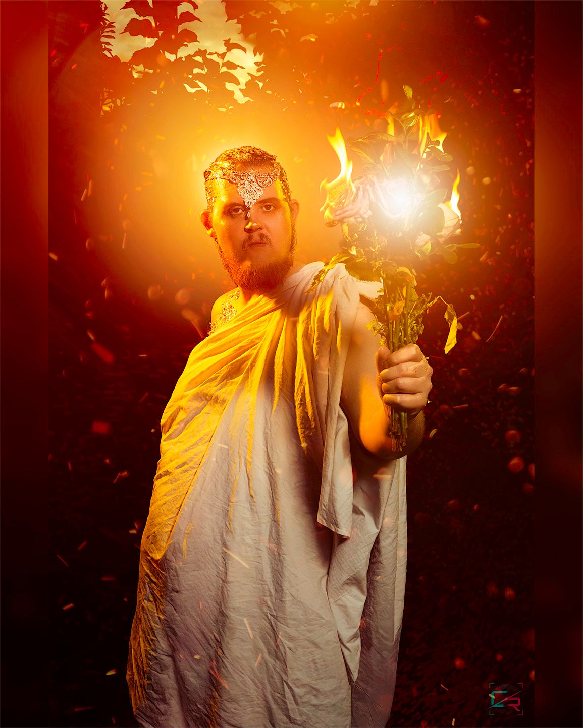 Man dressed as ancient deity holding flaming torch, surrounded by golden orange light and falling petals in mystical forest.