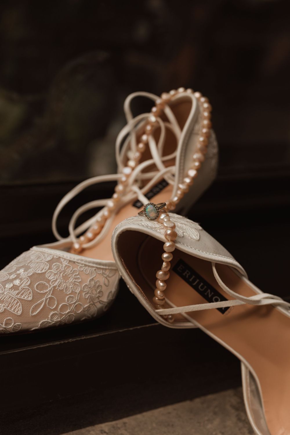 Elegant lace wedding shoes with pearl details on dark background.