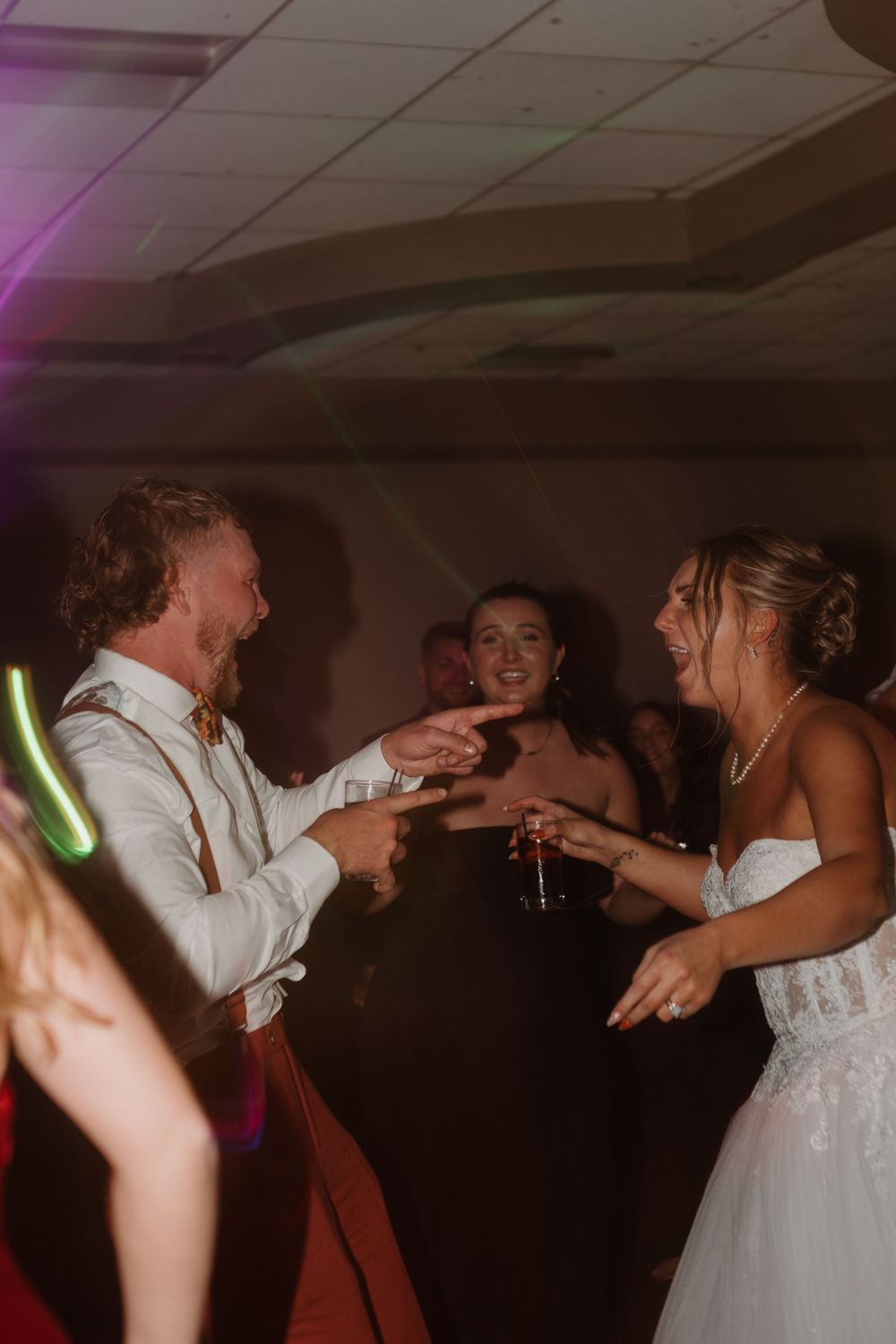Lively dance floor moments at wedding reception with dramatic lighting.