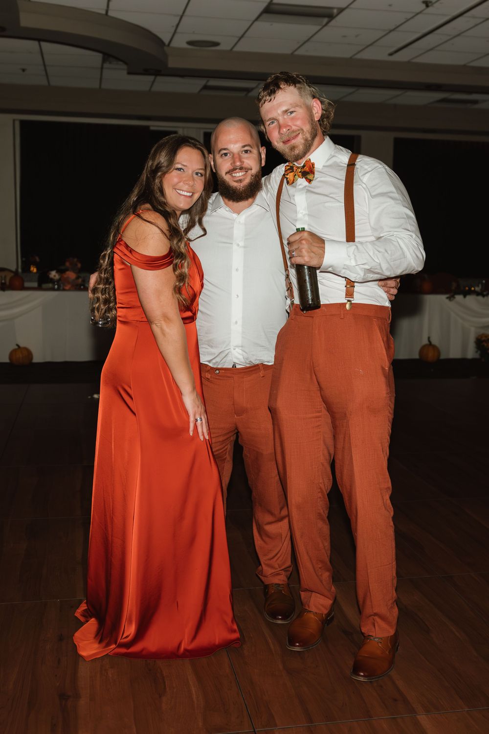 Wedding party in rust orange and white attire posing on dance floor.