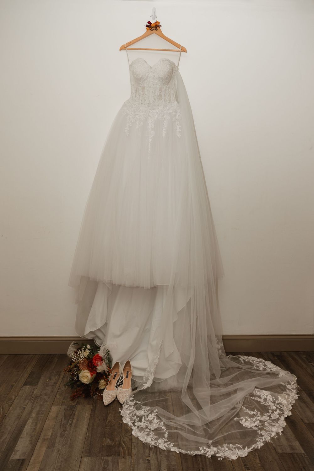 Elegant white wedding gown with lace details and long train displayed on wooden floor.