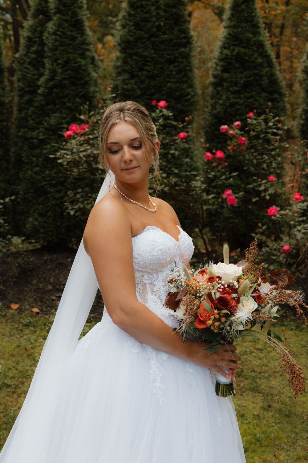 White ballgown wedding dress with sweetheart neckline and fall-inspired bouquet in outdoor setting.