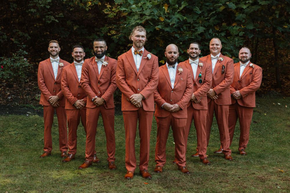 Groomsmen in matching rust-colored suits line up for formal wedding photo.