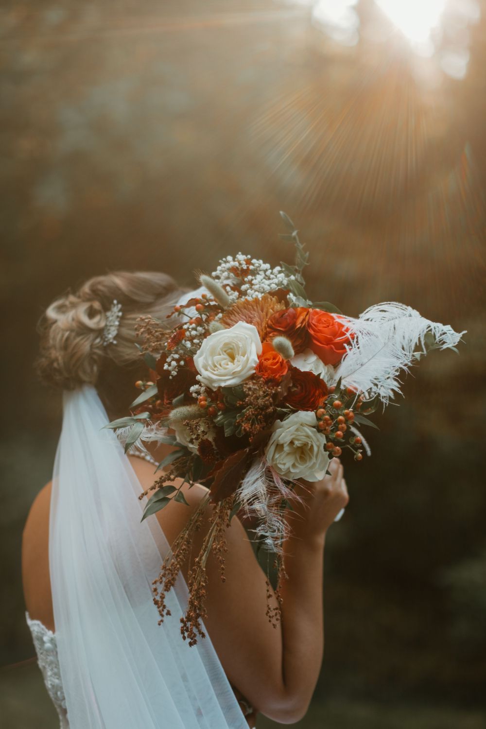 Delicate floral bouquet with white and coral flowers against a sunset backdrop with lens flare.