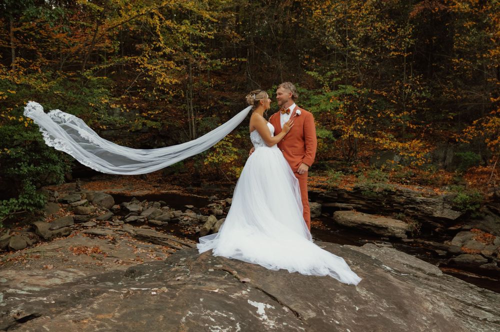 Flowing white wedding dress train cascades over rocky terrain in outdoor forest setting.