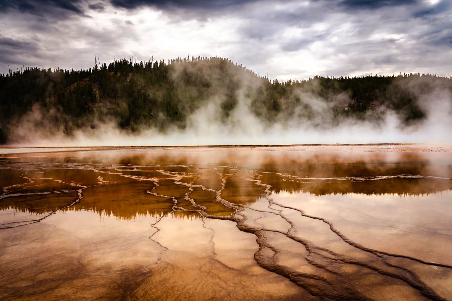 Steaming geothermal hot spring with golden mineral deposits creates otherworldly patterns at sunset.