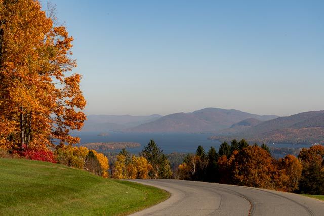 Winding mountain road through vibrant fall foliage with distant blue mountains under clear skies.