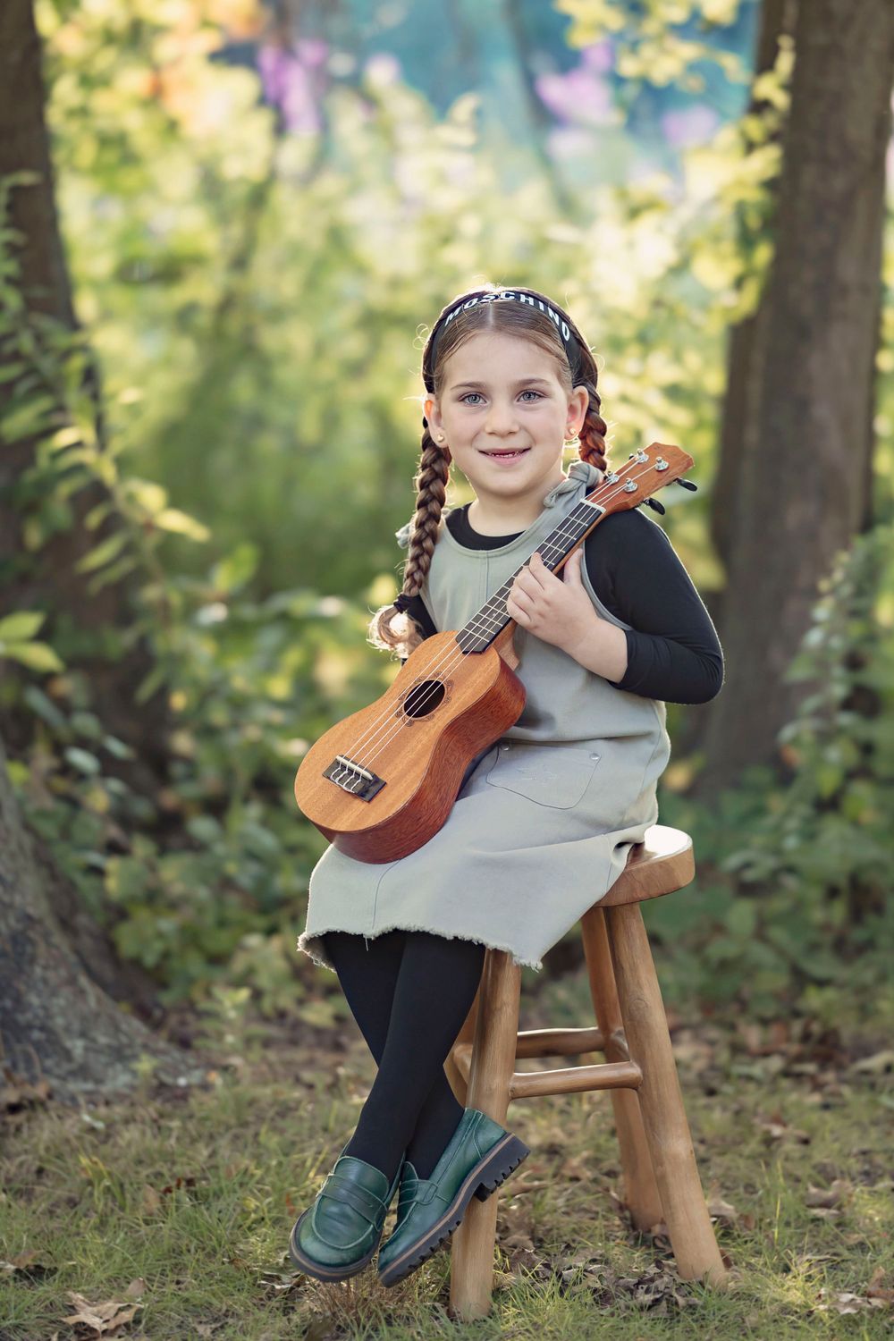 Child sitting on wooden stool playing ukulele/guitar in enchanted forest setting.