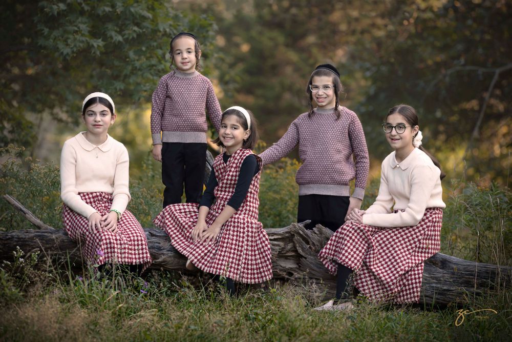 Group photo of children in coordinated outfits sitting on log in autumn setting.