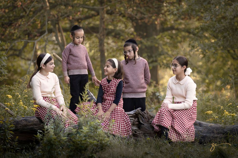 Children in matching pink sweaters and plaid skirts posed outdoors in autumn woods.