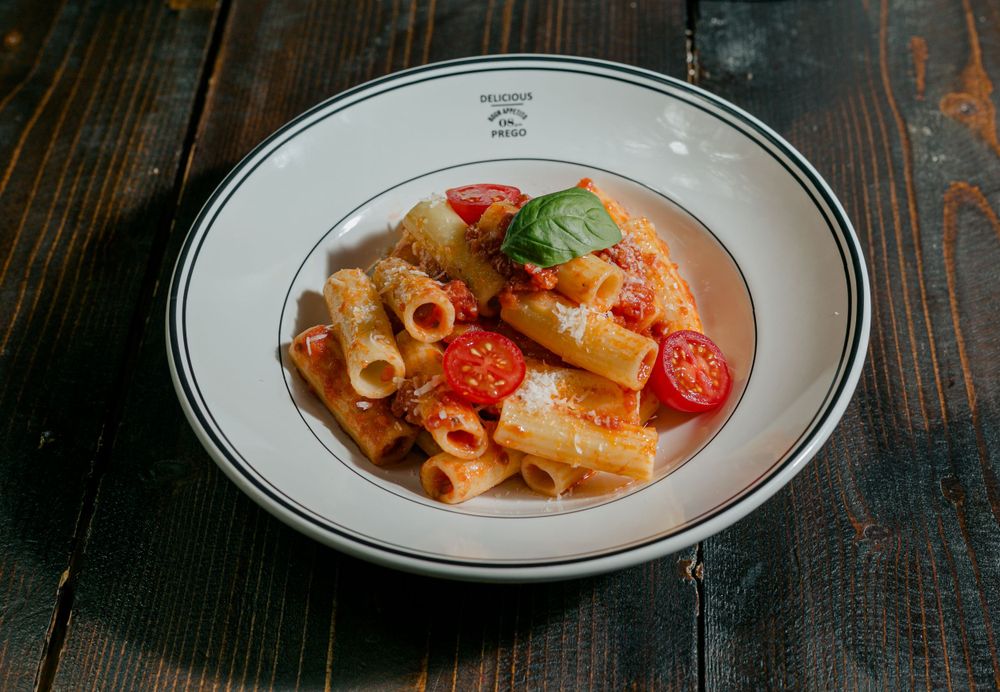 Rigatoni pasta with cherry tomatoes and basil served on white rimmed plate.