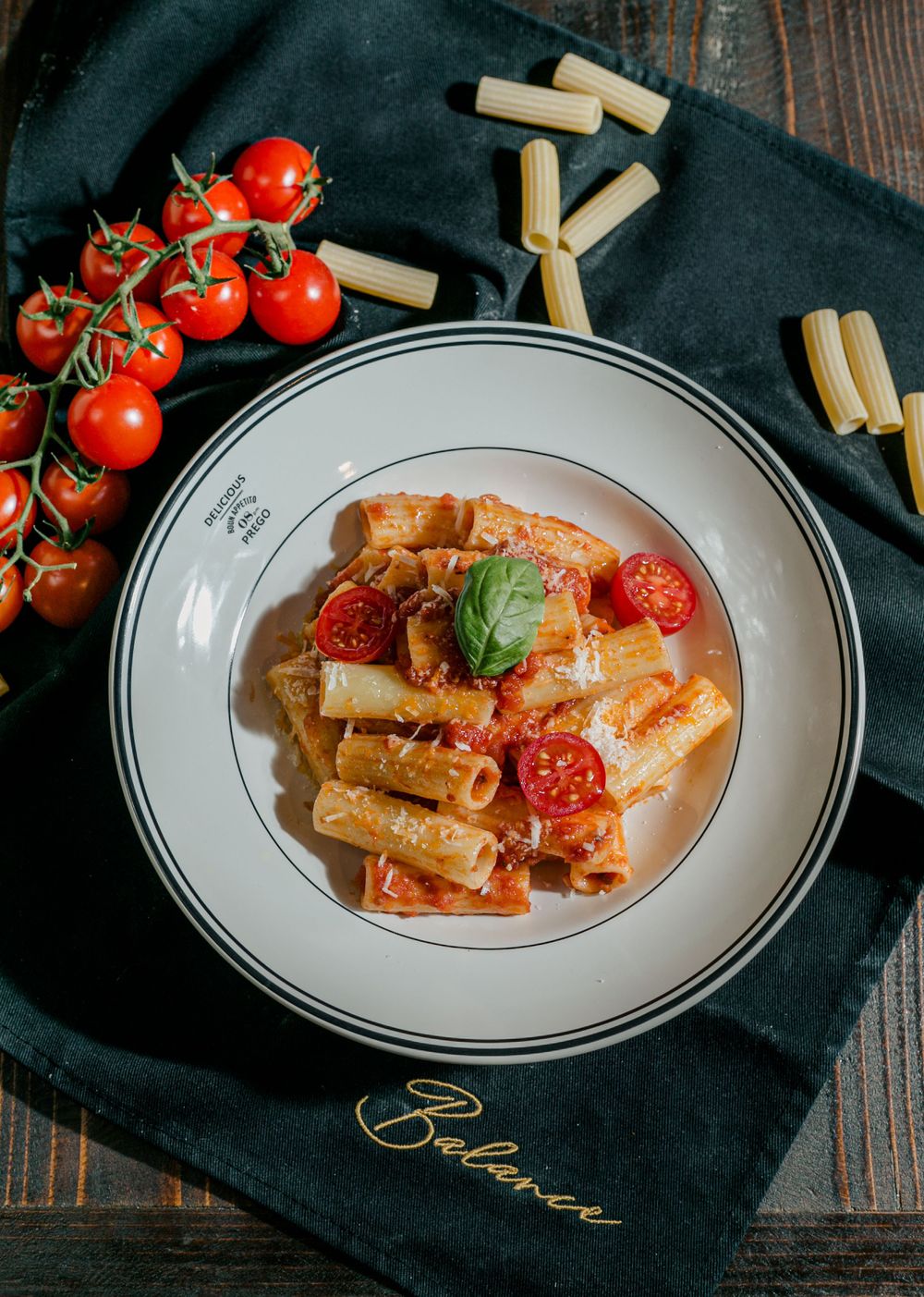 Rigatoni pasta with tomato sauce and cherry tomatoes served on white plate with black napkin.