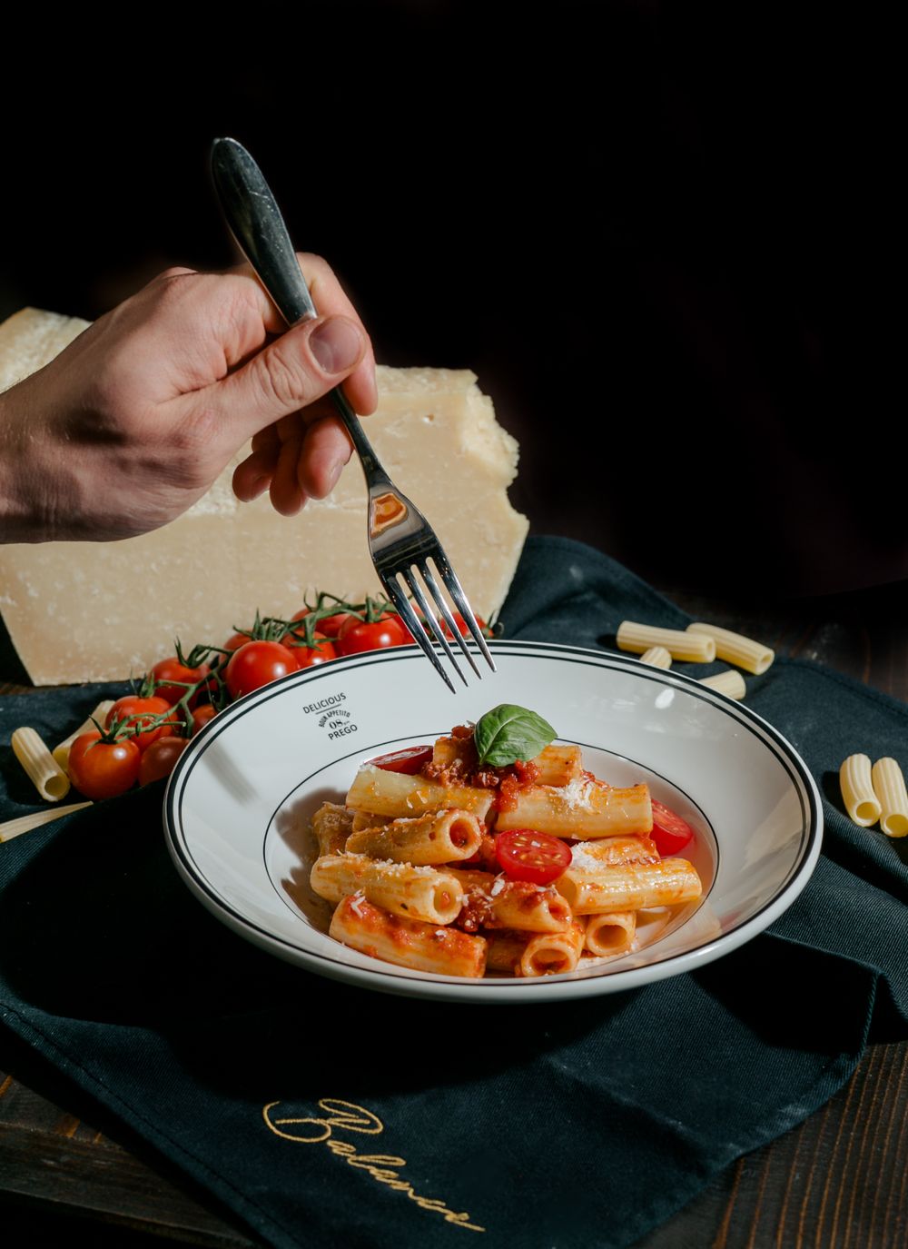 Rigatoni pasta with tomatoes and basil being eaten from white plate with fork.