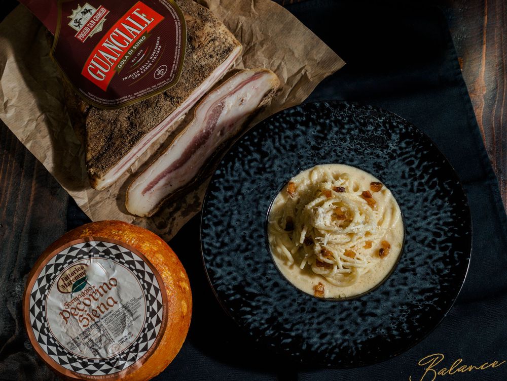 Carbonara pasta on black plate with bacon and cheese ingredients.